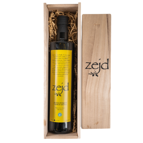 A bottle of Zejd extra virgin olive oil in a wooden gift box with shredded paper, shown next to its wooden lid on a white background.